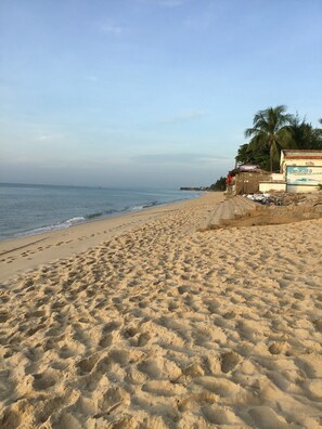 Una playa arenosa con huellas que conducen a un edificio con un letrero que dice "sankara kitesurfing academy".
