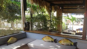 A seating area with a view of the outdoors, including a thatched roof structure and greenery. - The Bay Mui Ne (Mui Ne)