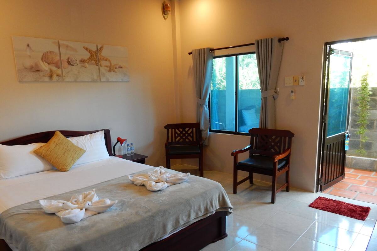 Habitación de hotel con cama, dos sillas, ventana con cortinas y puerta que da al exterior.