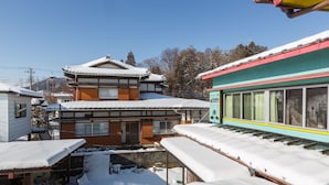A traditional Japanese building with a snow-covered roof and a colorful train station in the foreground. - Guesthouse Asobi Factory - Hostel (Fujikawaguchiko)