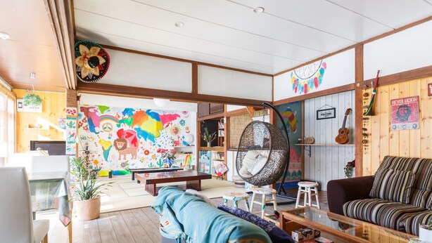 A cozy living room with a colorful mural, a hanging chair, a sofa, and a wooden bookshelf. - Guesthouse Asobi Factory - Hostel (Fujikawaguchiko)