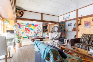 Un salon chaleureux agrémenté d’une fresque murale colorée, d’un fauteuil suspendu, d’un canapé et d’une bibliothèque en bois.