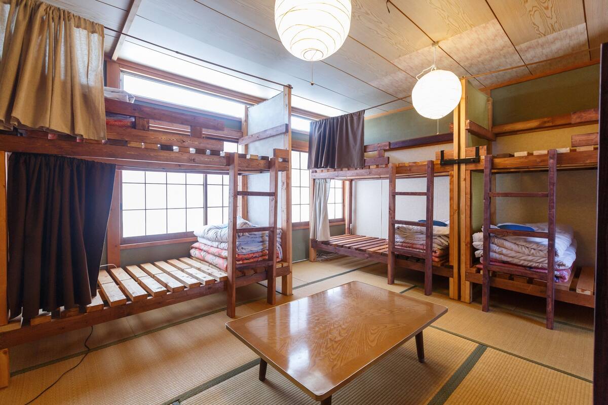 A traditional Japanese-style room with tatami flooring, wooden bunk beds, and a low table.
