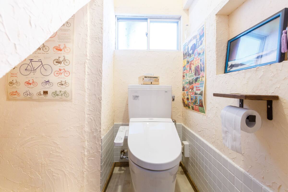 A small bathroom with a toilet, a window, and a wall-mounted toilet paper holder.