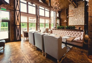 A spacious dining area with a long table, multiple chairs, and a plush sofa. Large windows provide natural light and views of the outdoors. - Eco-hotel Izumrudniy les (Nudol')