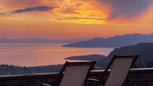 A sunset view from a balcony with lounge chairs, overlooking a calm body of water and distant mountains. - Rathimata villas (West Mani)
