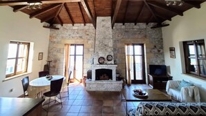A rustic interior with a stone fireplace, wooden beams, and a stone wall. - Rathimata villas (West Mani)