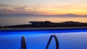 A swimming pool with metal railings, a view of a distant shoreline, and a sunset in the background. - Rathimata villas (West Mani)