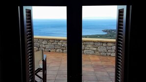 A view from a balcony with stone walls and a chair, overlooking a coastal area with buildings and the sea. - Rathimata villas (West Mani)