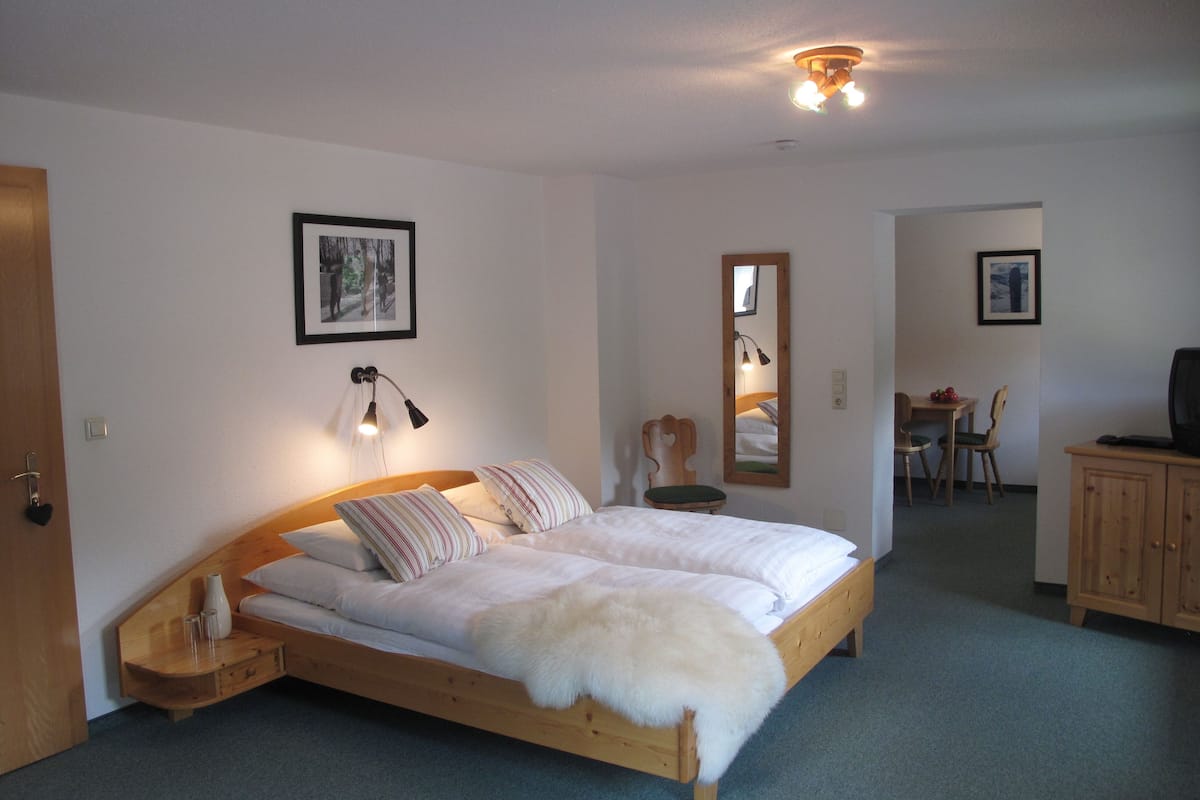 A bedroom with a wooden bed, a bedside table, a mirror, and a small desk with a chair.