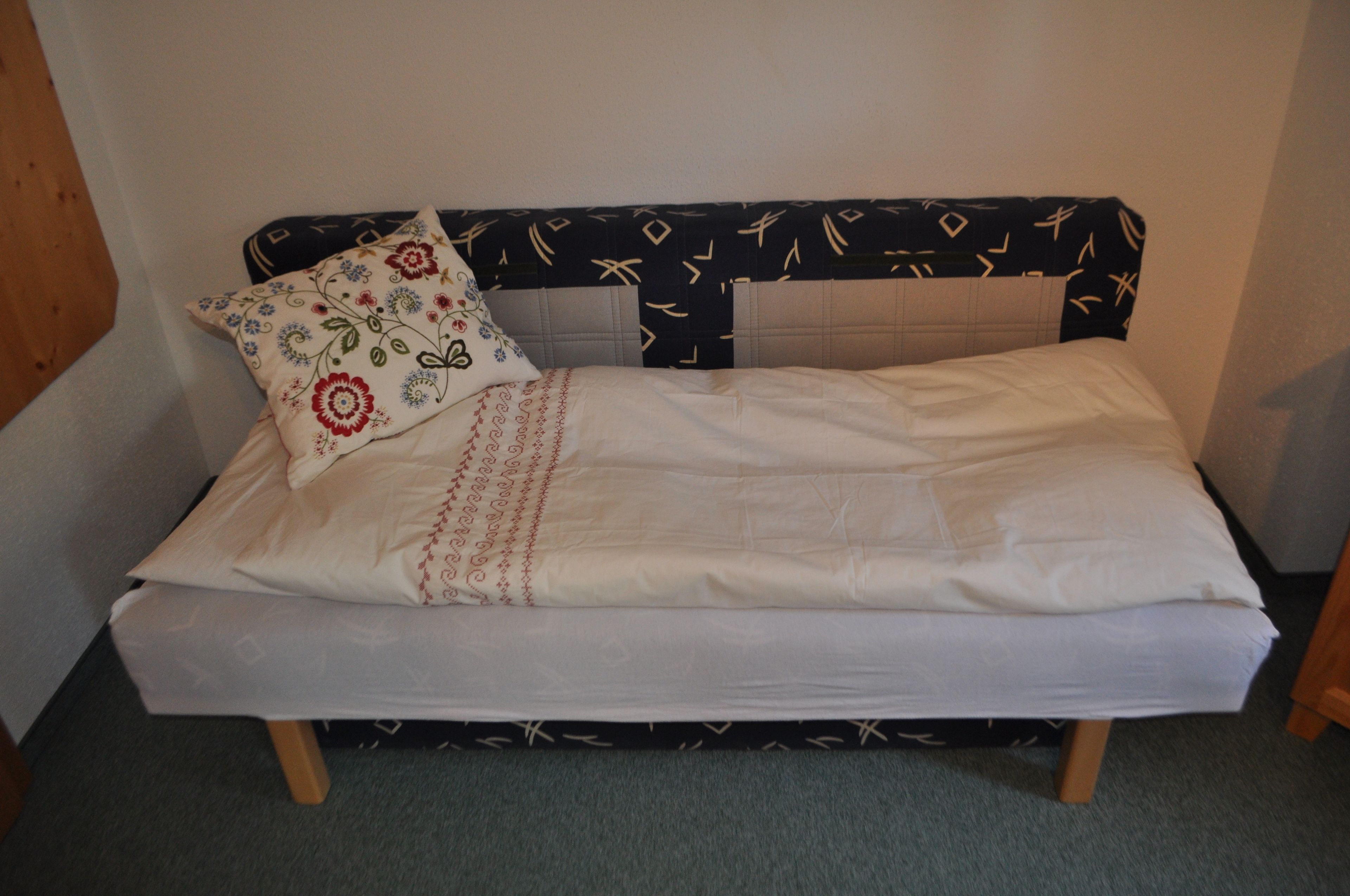 A small bed with a floral pillow and a white bedspread.