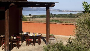 Eine Terrasse im Freien mit Holztischen und -stühlen, Blumentöpfen und Blick auf das Meer und die Hügel.
