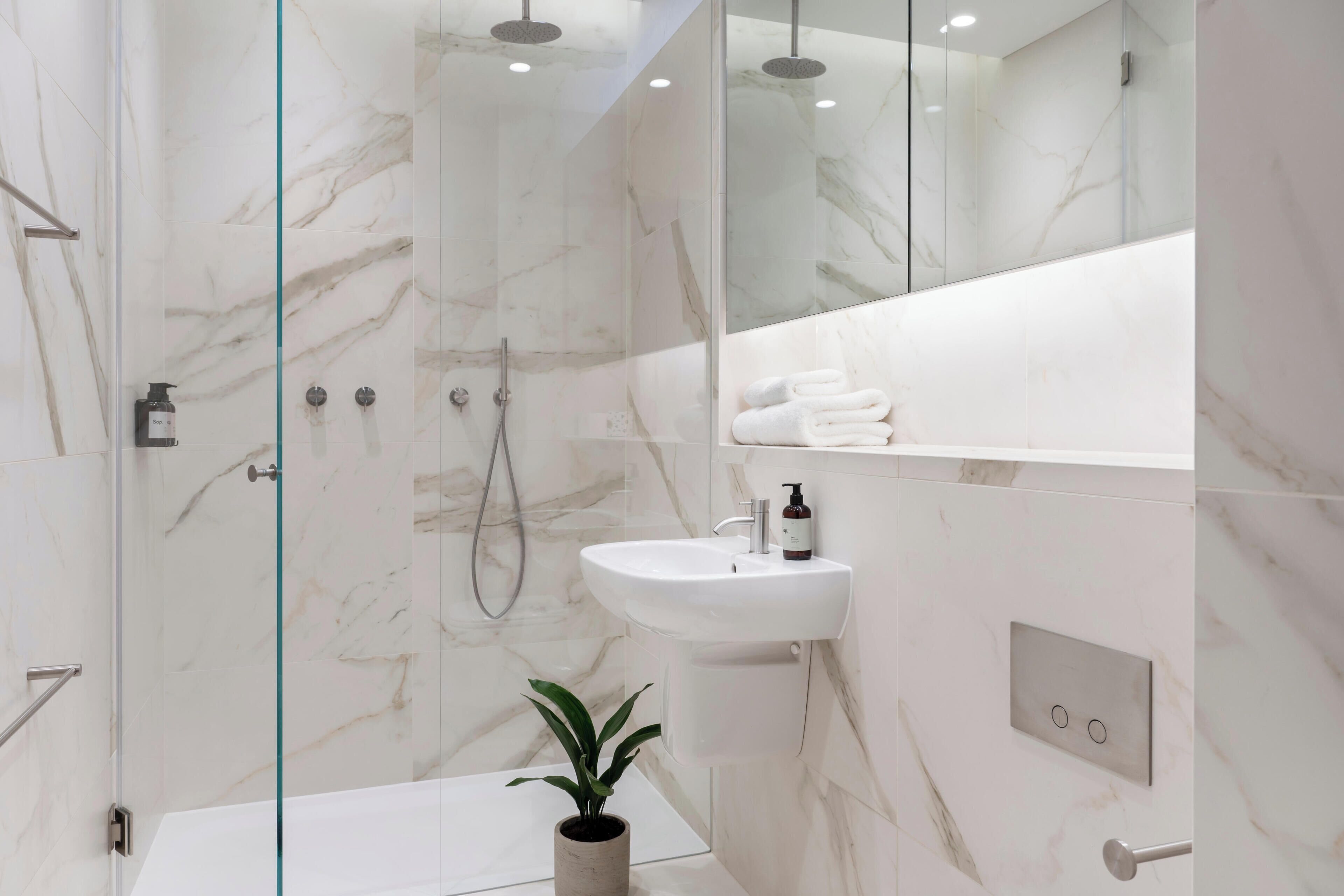 A modern bathroom with a glass-enclosed shower, a white sink, and a marble-tiled wall.