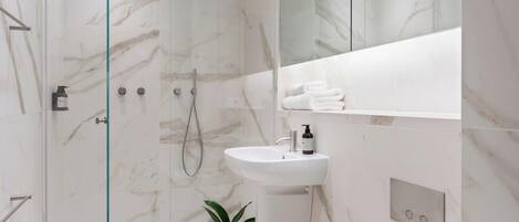 A modern bathroom with a glass-enclosed shower, a white sink, and a marble-tiled wall.