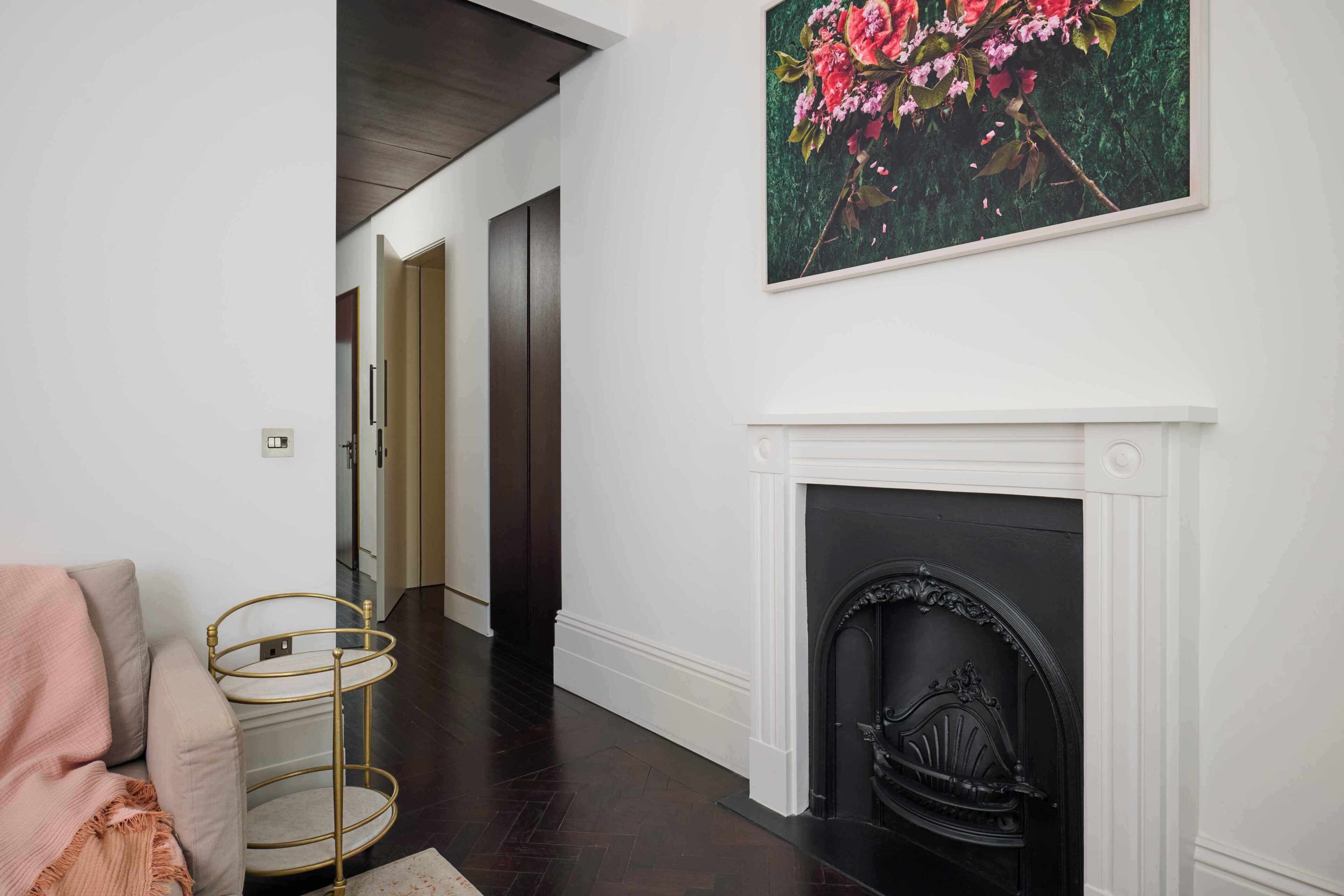 A hallway with a white fireplace, a painting of flowers, and a multi-tiered metal stand.