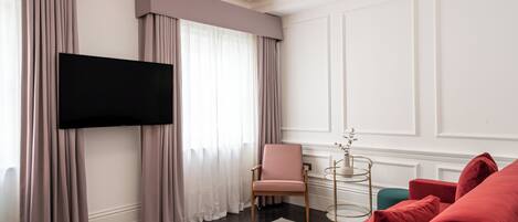 A modern living room with a flat-screen TV mounted on the wall, a pink armchair, a red sofa, and a small side table with a vase.