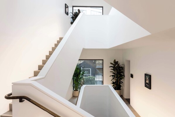 A modern staircase with a straight design, leading to a landing area with a view of the outside. - The Moorgate by Cove (London)