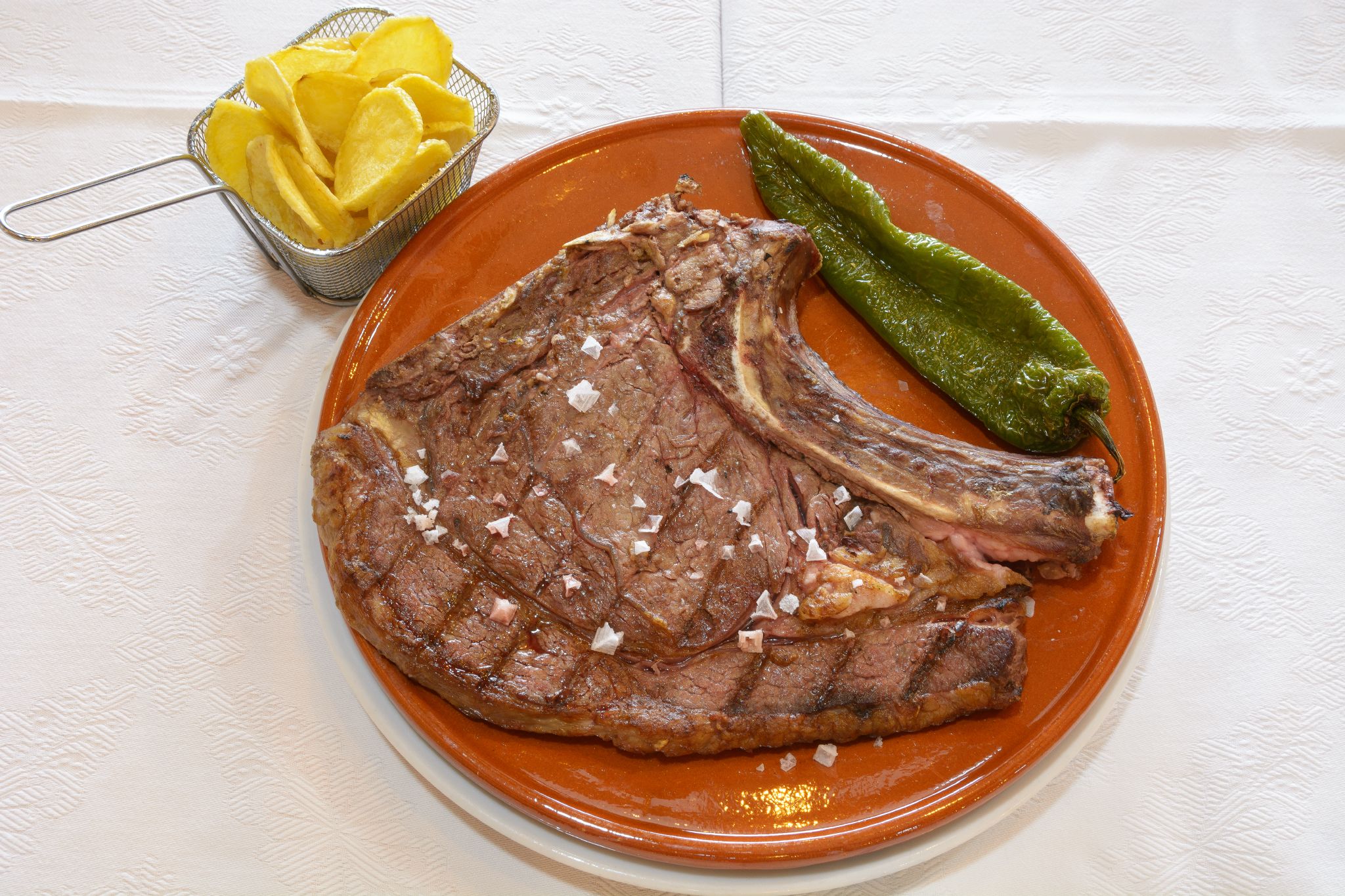 Un plato con un filete a la parrilla, un chile verde y una cesta pequeña de totopos amarillos.