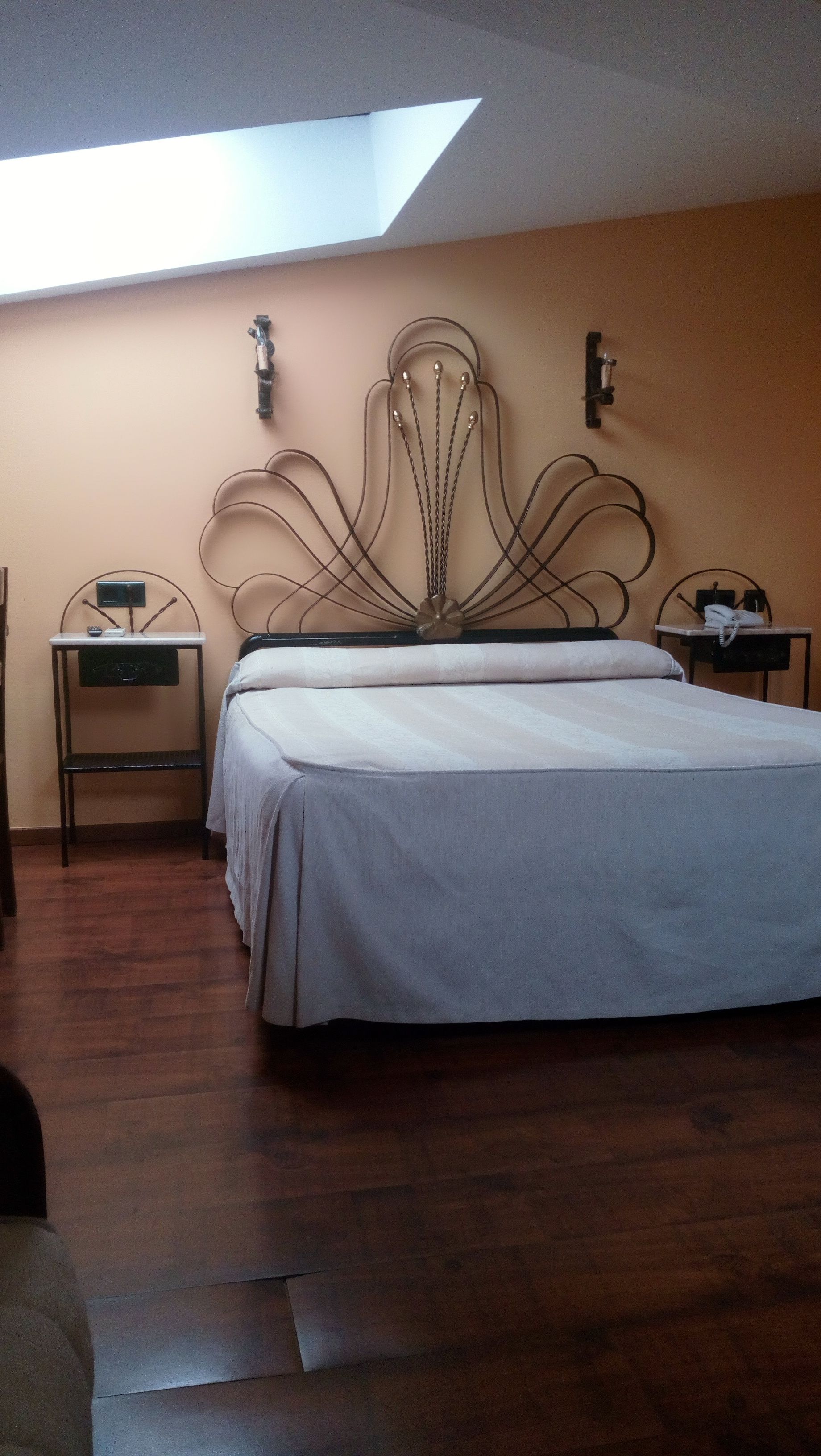 A bedroom with a bed, a desk, and a chair. There is a skylight above the bed.