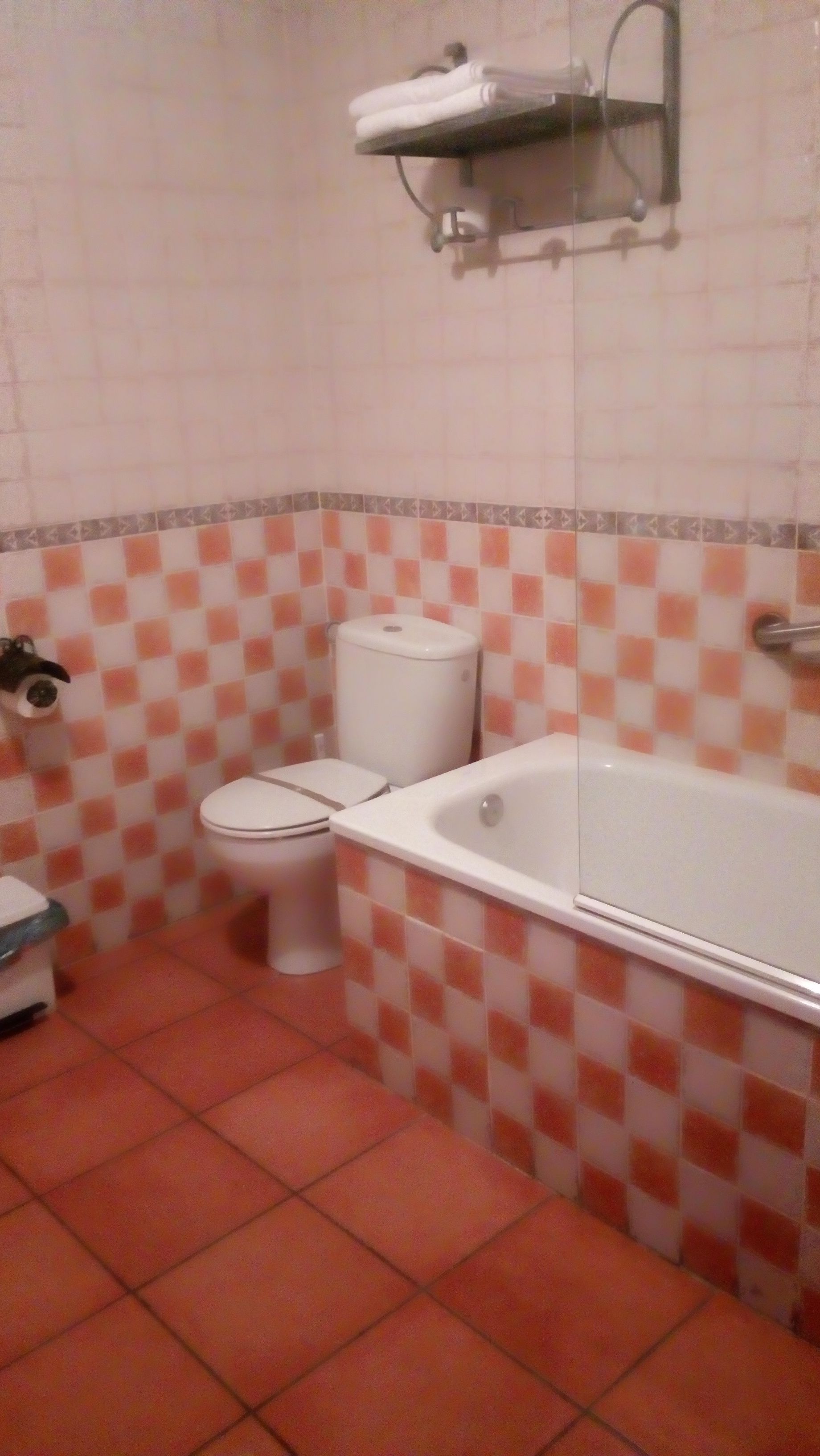 A bathroom with a toilet, a bathtub, and a shelf with towels.