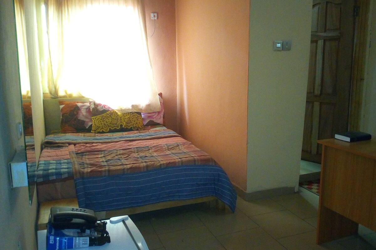 A small, compact room with a single bed, a desk, and a chair.