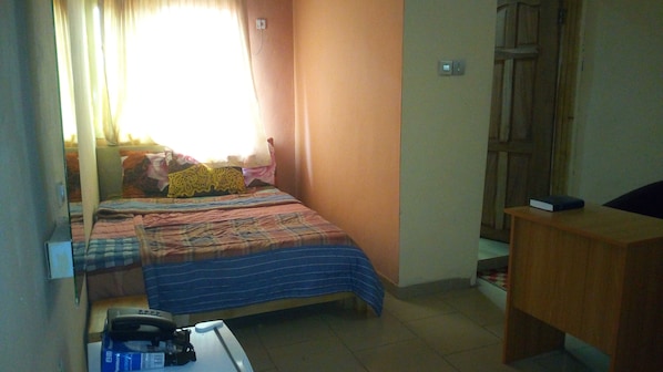A small, compact room with a single bed, a desk, and a chair.