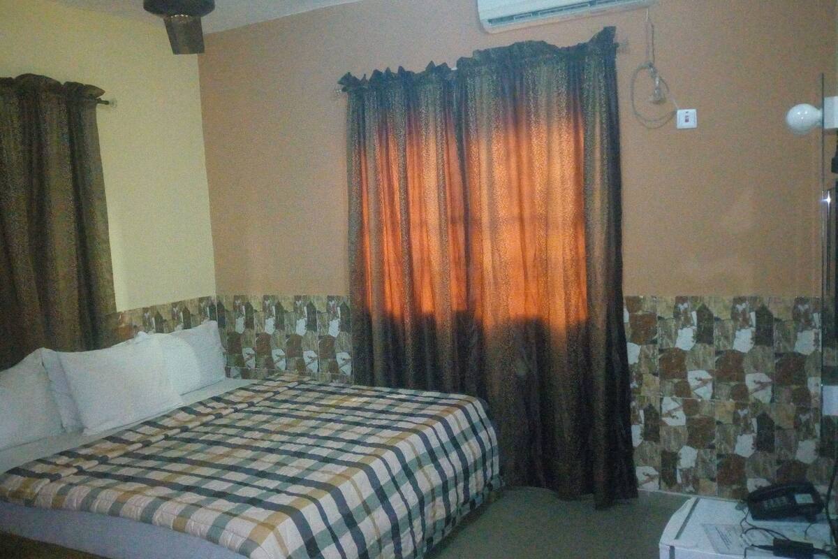 A hotel room with a bed, curtains, an air conditioning unit, and a tiled wall.