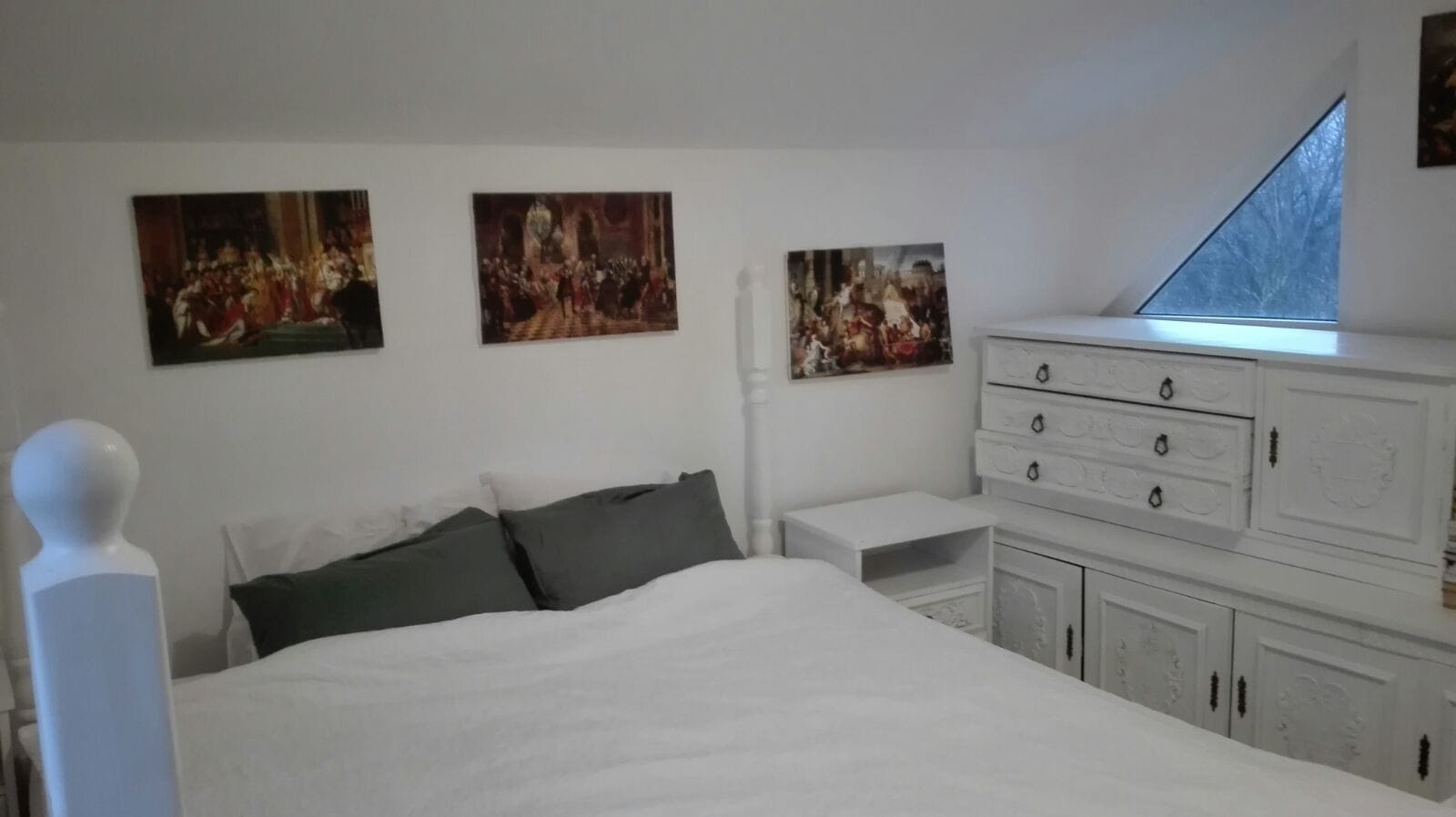 Un dormitorio con una cama grande, un aparador y tres cuadros en la pared.