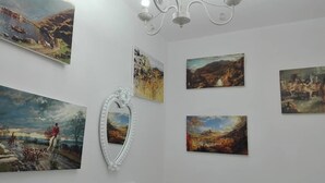 A gallery with six paintings on the wall, a white decorative mirror, and a chandelier.