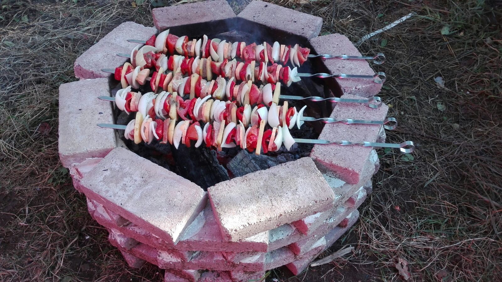 A barbecue grill made of bricks with skewers of meat and vegetables.