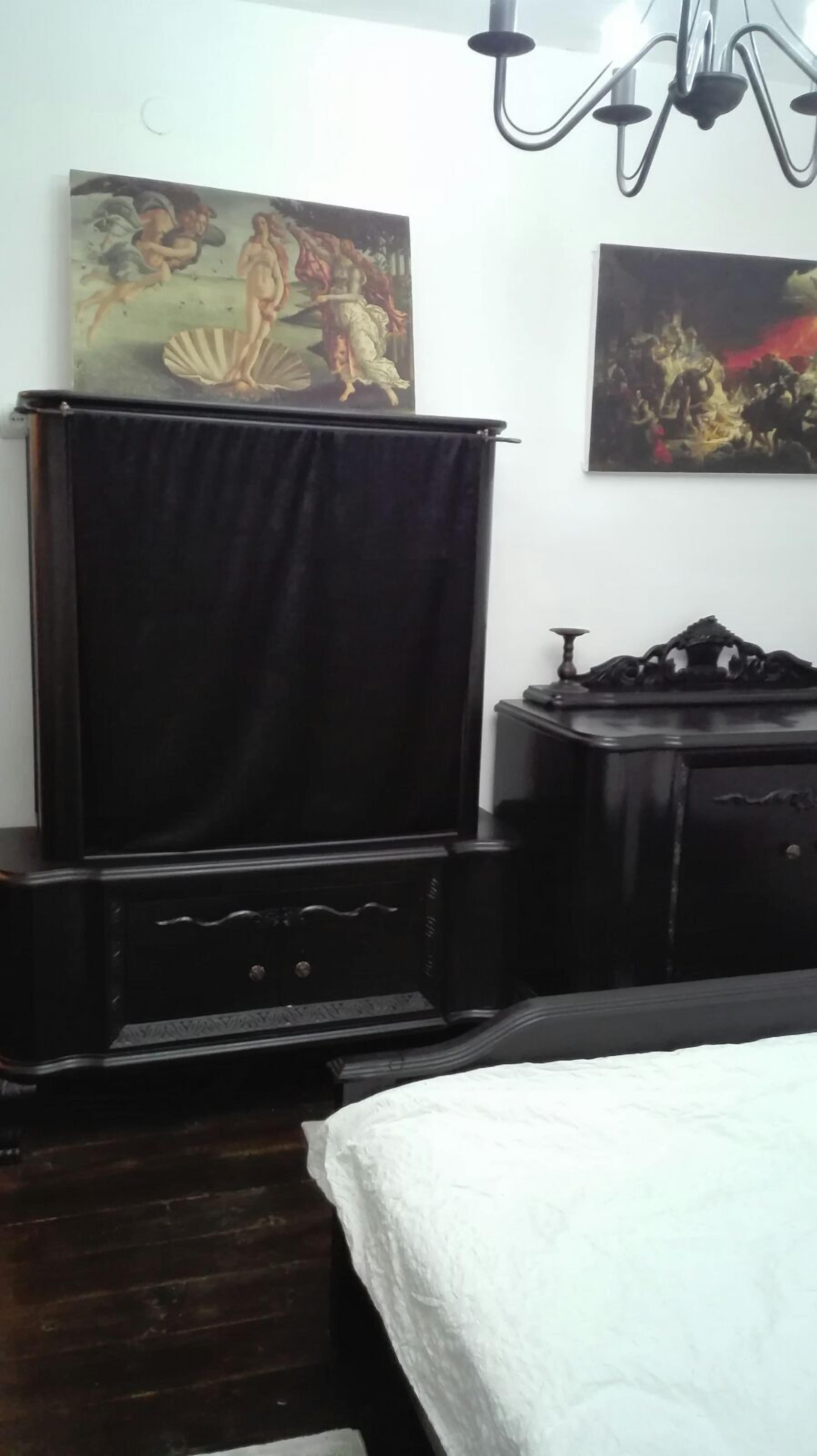 A bedroom with a bed, a dark wooden dresser, a TV on a stand, and two paintings on the wall.