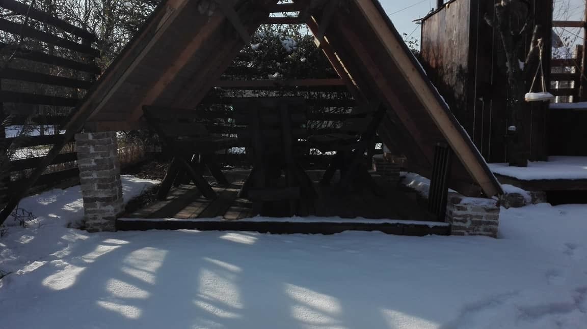 Un espace extérieur enneigé, avec une structure en bois, peut-être un pont ou une passerelle, et un réservoir ou un conteneur métallique en arrière-plan.