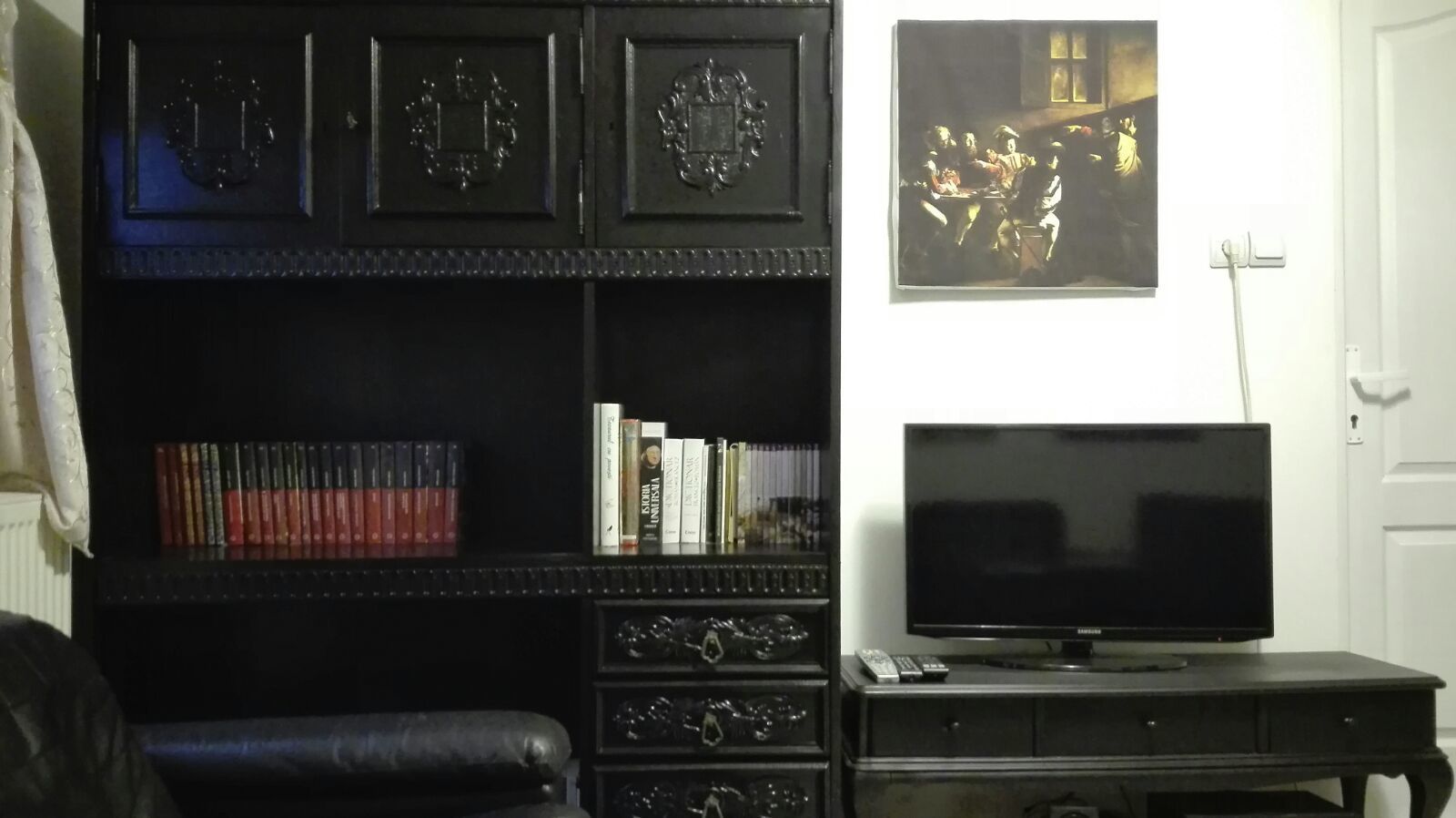 A living room with a black entertainment unit, a flat-screen TV, and a bookshelf.