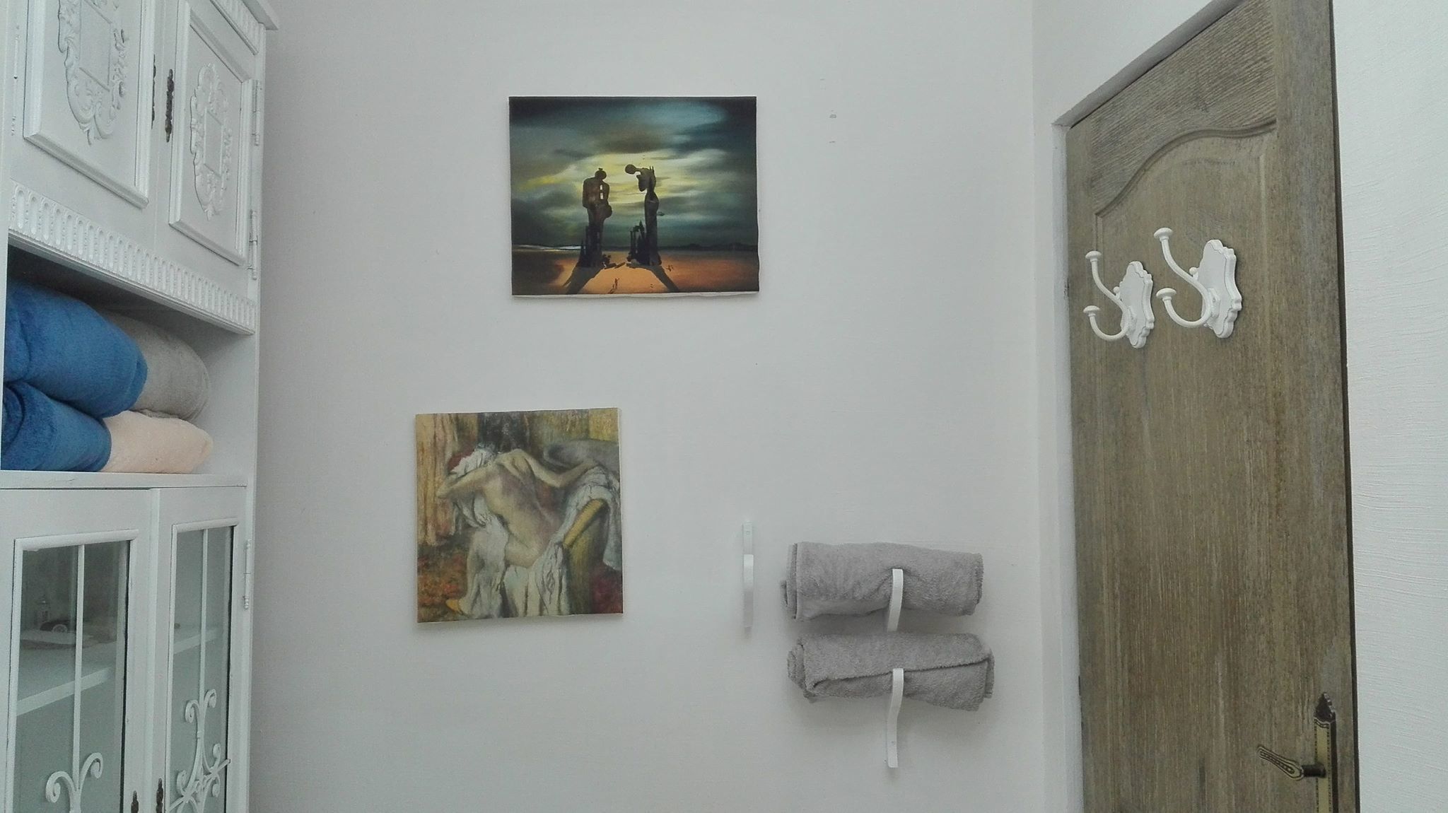 Una habitación con un armario blanco, un cuadro de dos figuras y un cuadro más pequeño.