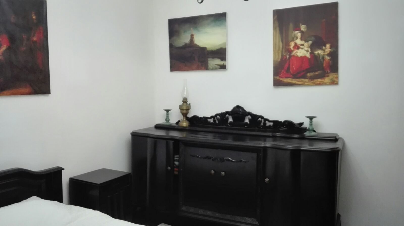 Un dormitorio con una cama, un aparador de madera oscura y tres cuadros en la pared.