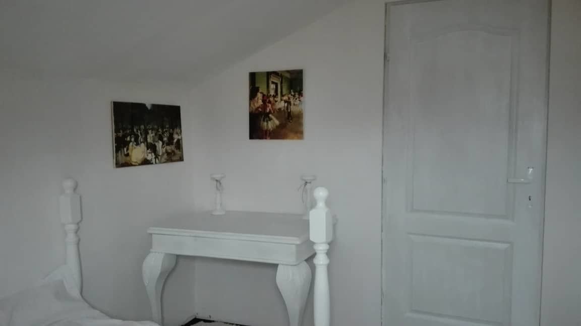 Una habitación con una puerta blanca, un tocador blanco con espejo, y dos cuadros en la pared.