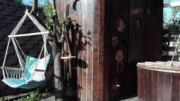 A hammock chair hanging from a tree, a wooden structure with circular cutouts, and a wooden bench.