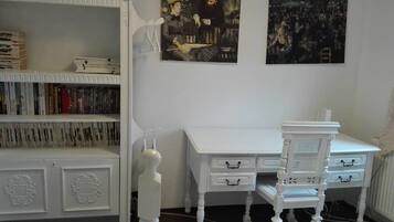 Een kamer met een witte boekenkast, een wit bureau met lades, en twee schilderijen aan de muur.