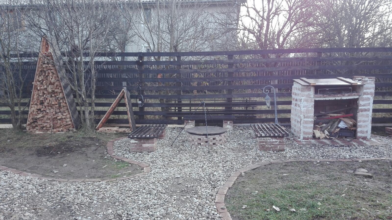 Un jardin avec une clôture en bois, un foyer en briques et une petite construction en briques.