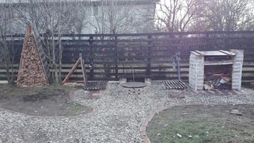 Un jardin avec une clôture en bois, un foyer en briques et une petite construction en briques.