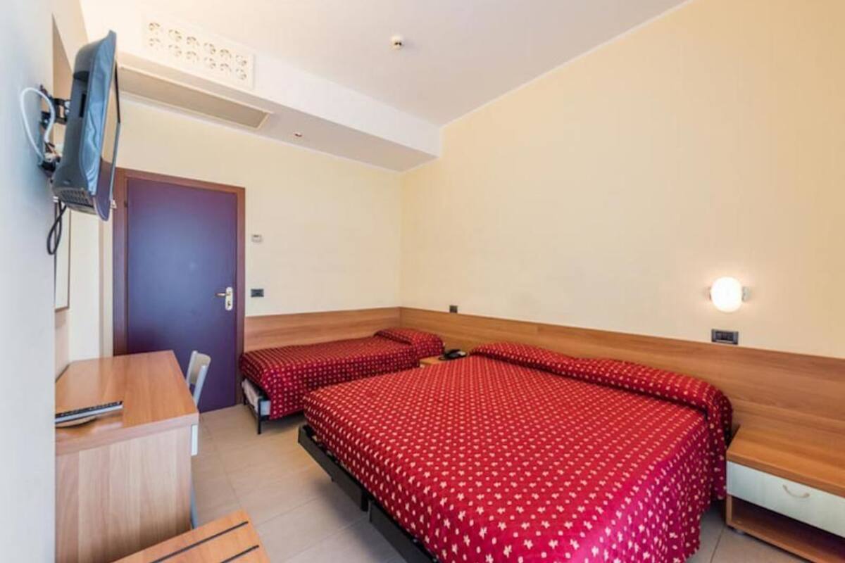 A hotel room with two beds, a desk, a chair, and a television.
