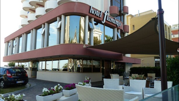A hotel with a curved facade, outdoor seating area, and a sign reading "hotel flamingo".