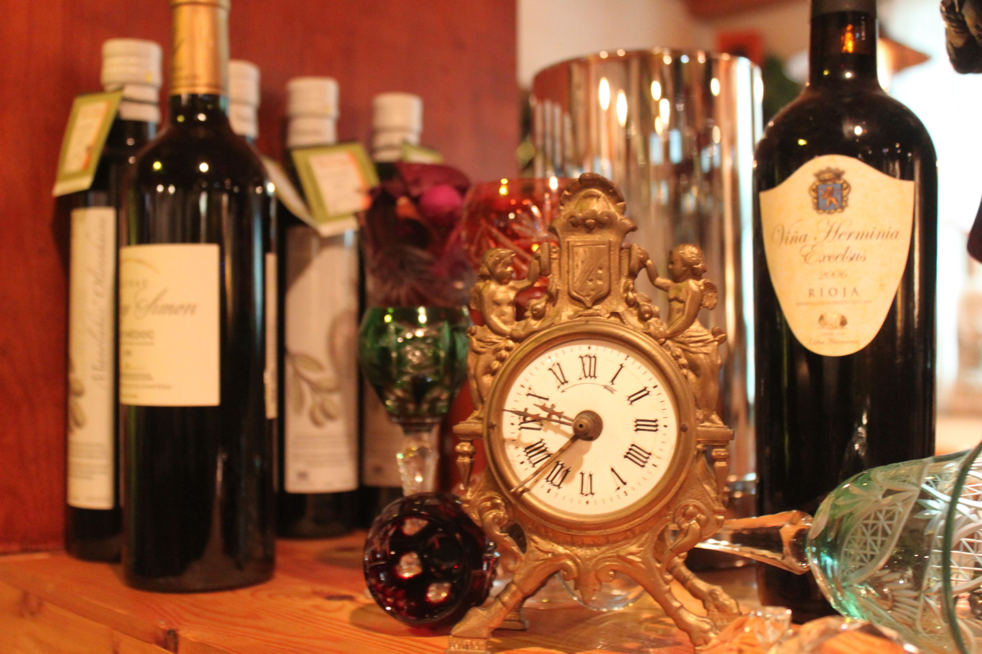 A collection of wine bottles and a decorative clock on a wooden surface.