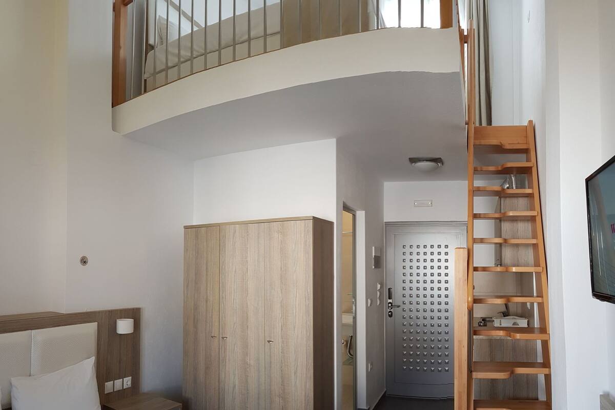 Ein Schlafzimmer mit einem Bett, einem Kleiderschrank, einer Holzleiter und einer Tür zu einem anderen Raum.