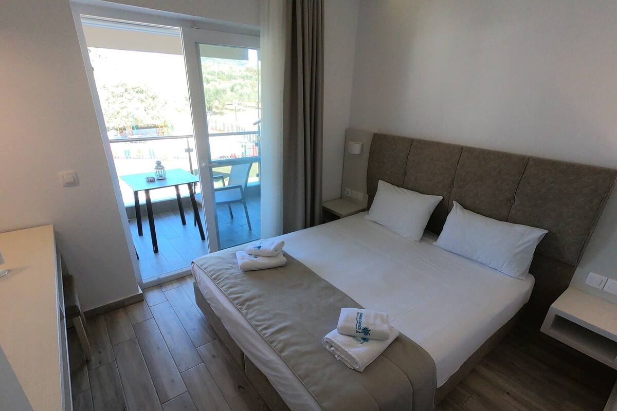 Ein Hotelzimmer mit Bett, Nachttisch, Schreibtisch und Blick ins Freie.
