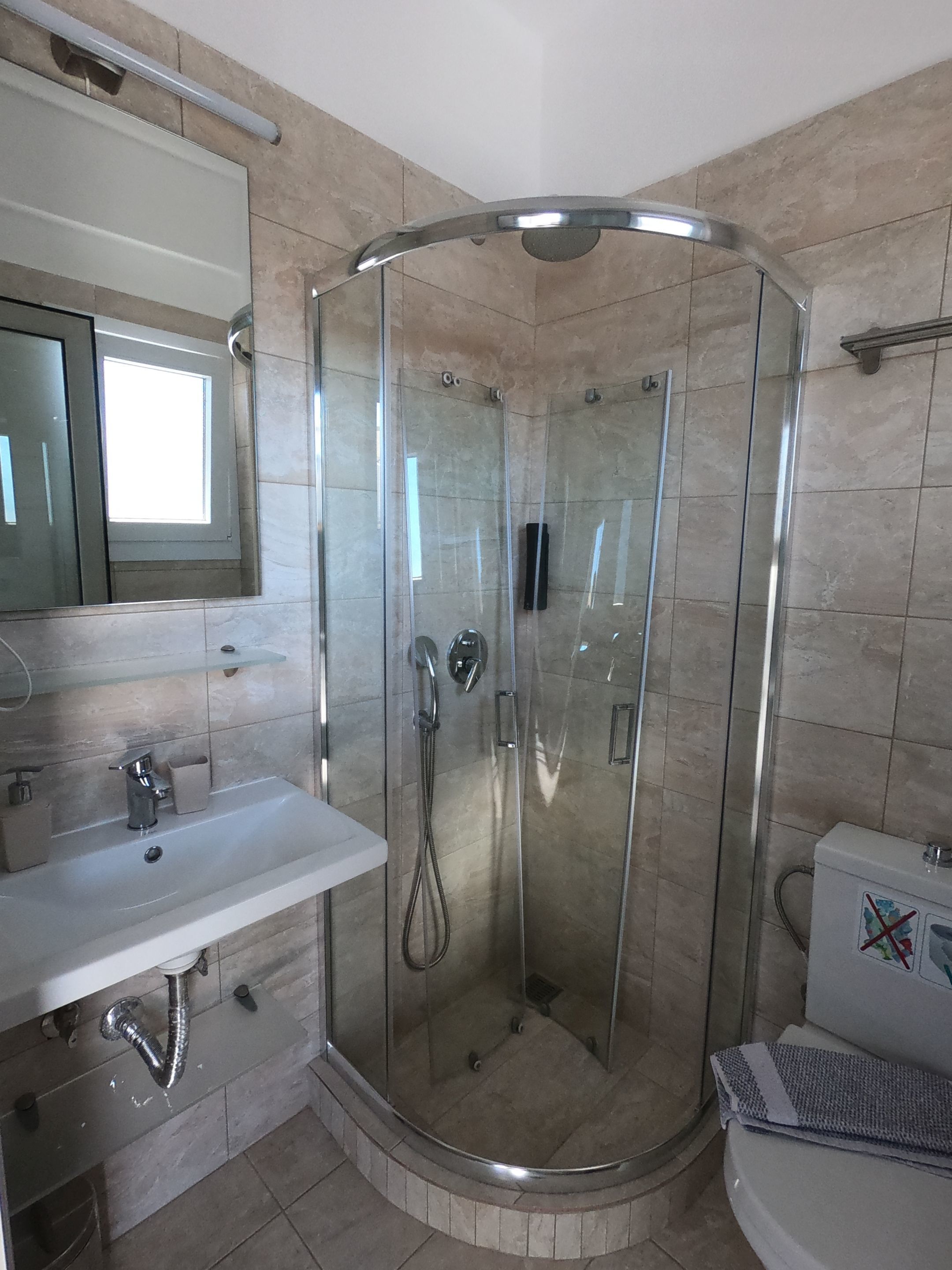 A modern bathroom with a glass-enclosed shower, a sink with a mirror, and a toilet.