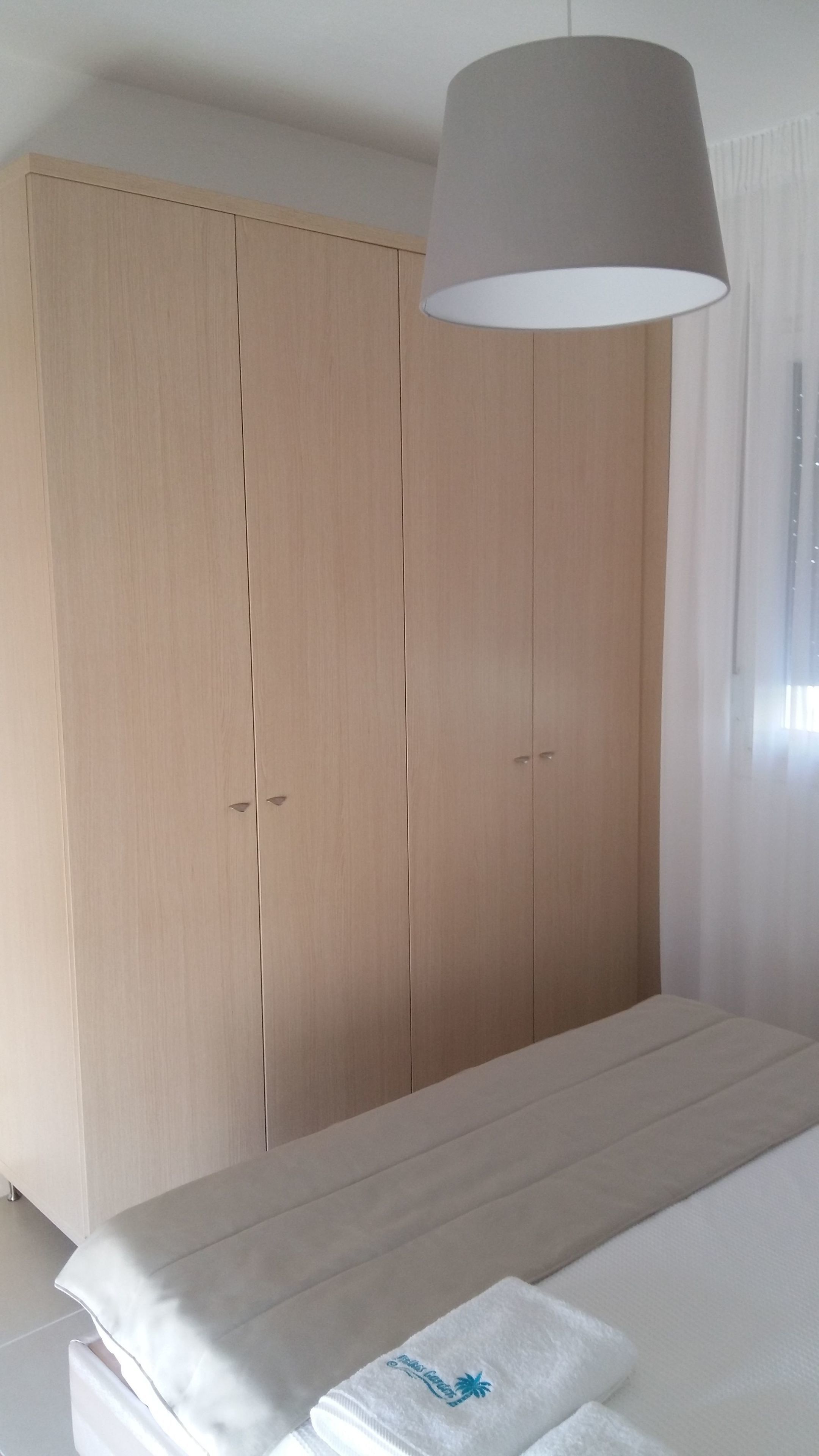 A bedroom with a large wardrobe, a bed with a white mattress, and a hanging lamp.