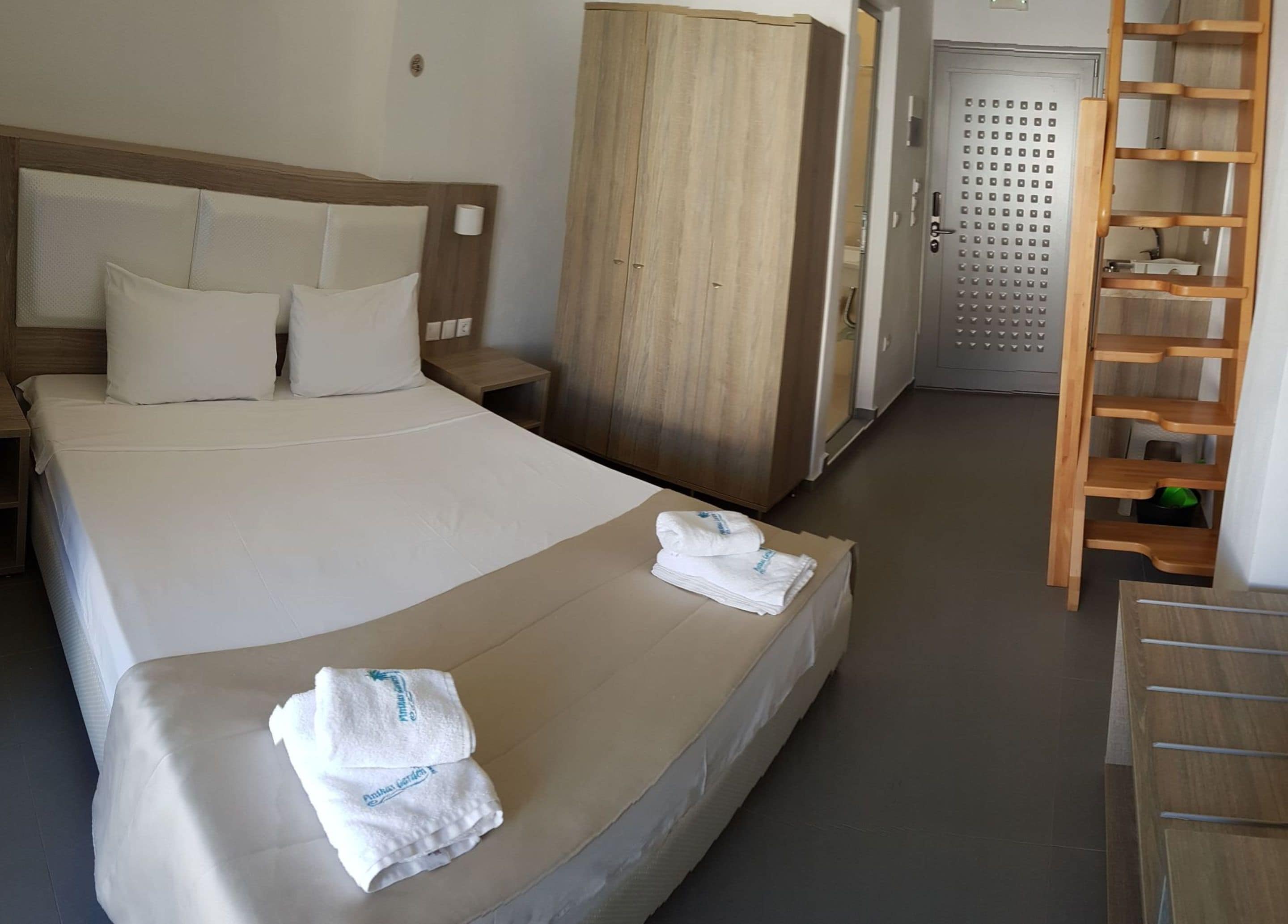 A hotel room with a large bed, a wooden wardrobe, a desk, and a wooden ladder.