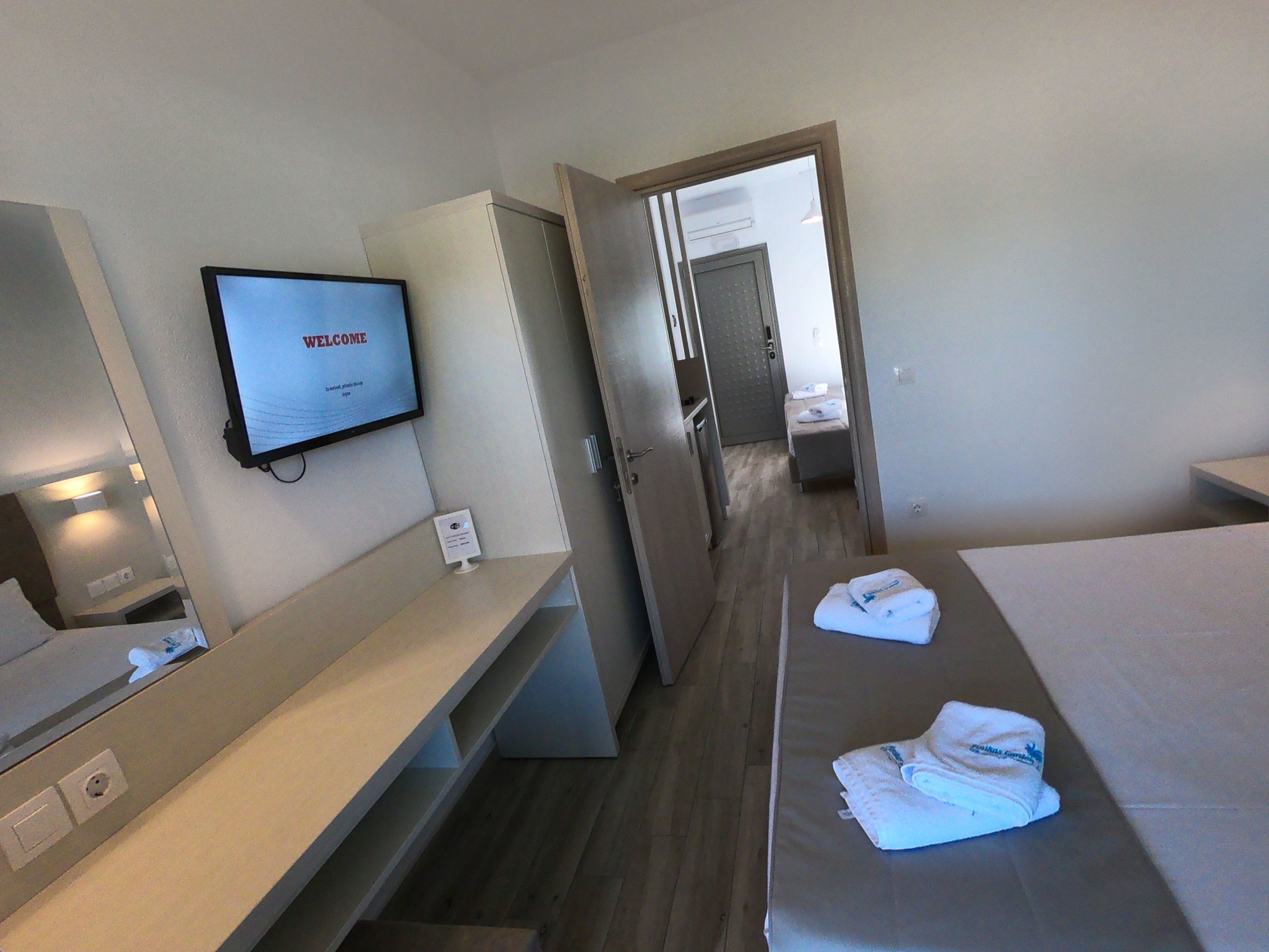 Hotelkamer met een bed, een bureau, een televisie waarop een welkomstbericht staat en een badkamer zichtbaar door een geopende deur.
