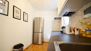 Een kleine keuken met een roestvrijstalen koelkast, een houten vloer en een aanrecht met diverse spullen.